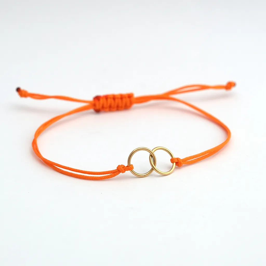 armband_aus_nylonband_orange_geknotet_an_mittelteil_2_ringe_ineinander_gehaengt_gelbgold